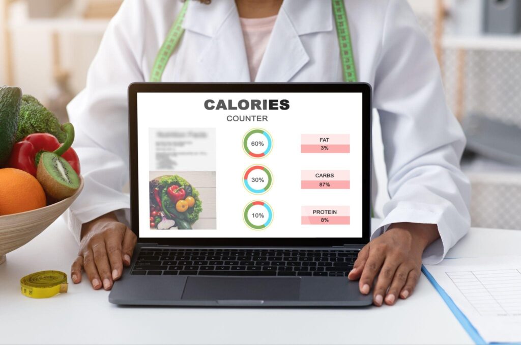 Nutritionist showing calorie counter on laptop with macronutrient breakdown. 