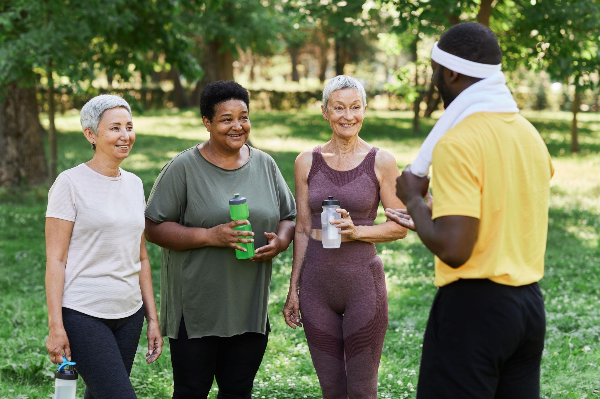 Senior women talking with a fitness coach during a group workout at a weight loss center outdoors