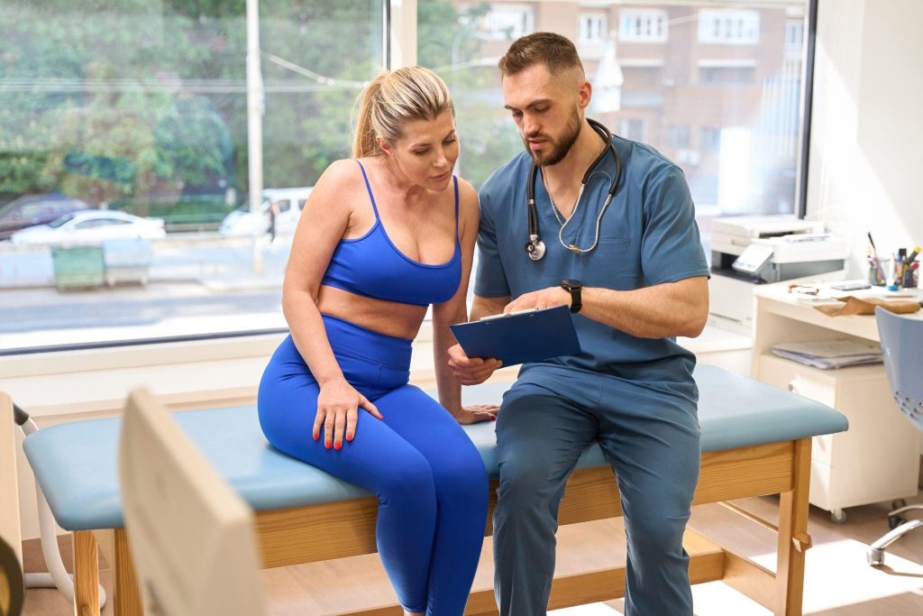 A woman in activewear speaking with a male doctor in a clinic, symbolizing professional weight loss consultations and personalized guidance.