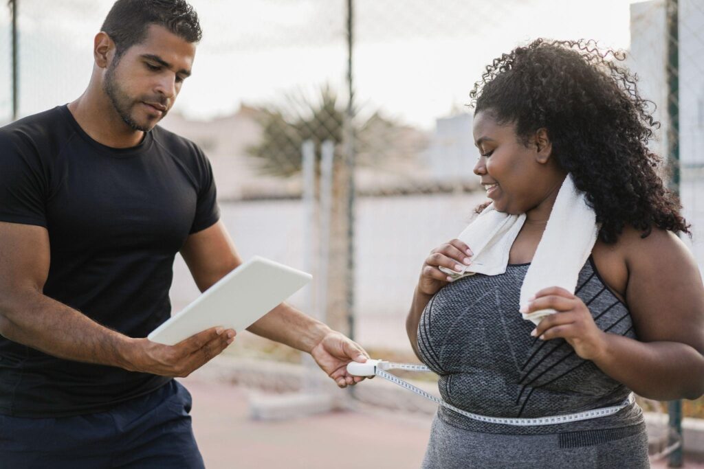 A woman smiling during a body measurement session with a fitness coach outdoors, representing support and progress at a weight loss center in Wilmington NC.