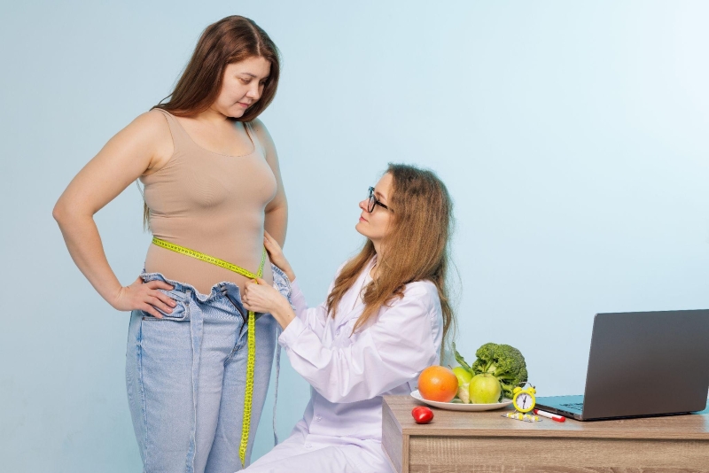 Weight loss specialist measuring a woman's waist during a consultation at a Wilmington weight loss clinic, with fresh fruits and vegetables on the desk.