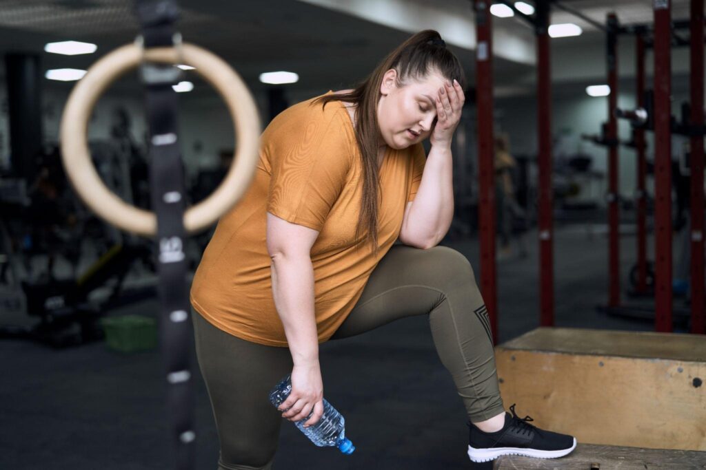 Tired woman at the gym feeling overwhelmed and exhausted after workout, showing why many in Wilmington need a smarter weight loss approach.